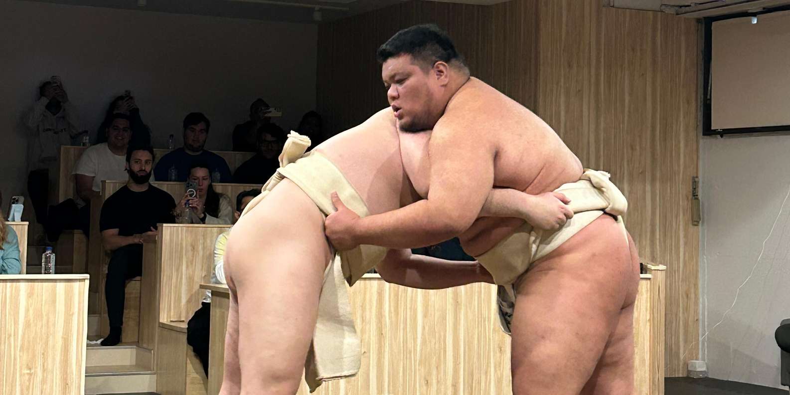 Tourist photographing professional sumo wrestlers during live sparring match demonstration at Shinjuku Tokyo experience venue highly recommended by Nicola from UK